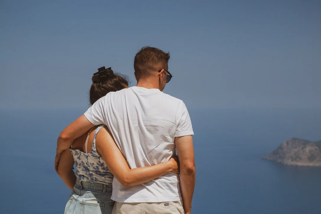 Twee mensen van achteren, arm in arm, uitkijkend over zee